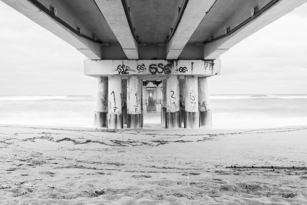 Una foto in bianco e nero di una spiaggia sotto un ponte