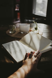 a person's hand holding an open book on a table