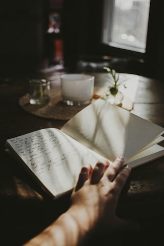 a person's hand holding an open book on a table