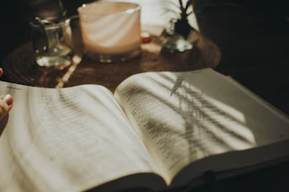 A cozy workspace with a lit candle and an open book on a wooden table.