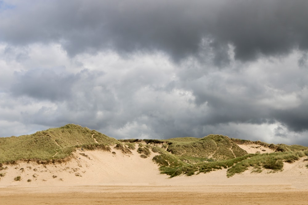 a sandy beach with a hill of sand and a cloudy sky