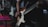 A person playing an electric guitar, focusing on the hand strumming the strings. The guitar is a classic sunburst design and the scene is dimly lit, suggesting a performance or practice environment. The blurry background indicates a stage or music venue setting.