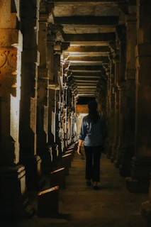 Cinematic moment frozen in time: a masked nomad walking through an ethereal, shadowy corridor framed with glowing gold accents.