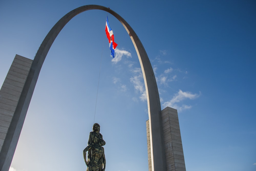 a statue of a man flying a kite in front of a large arch