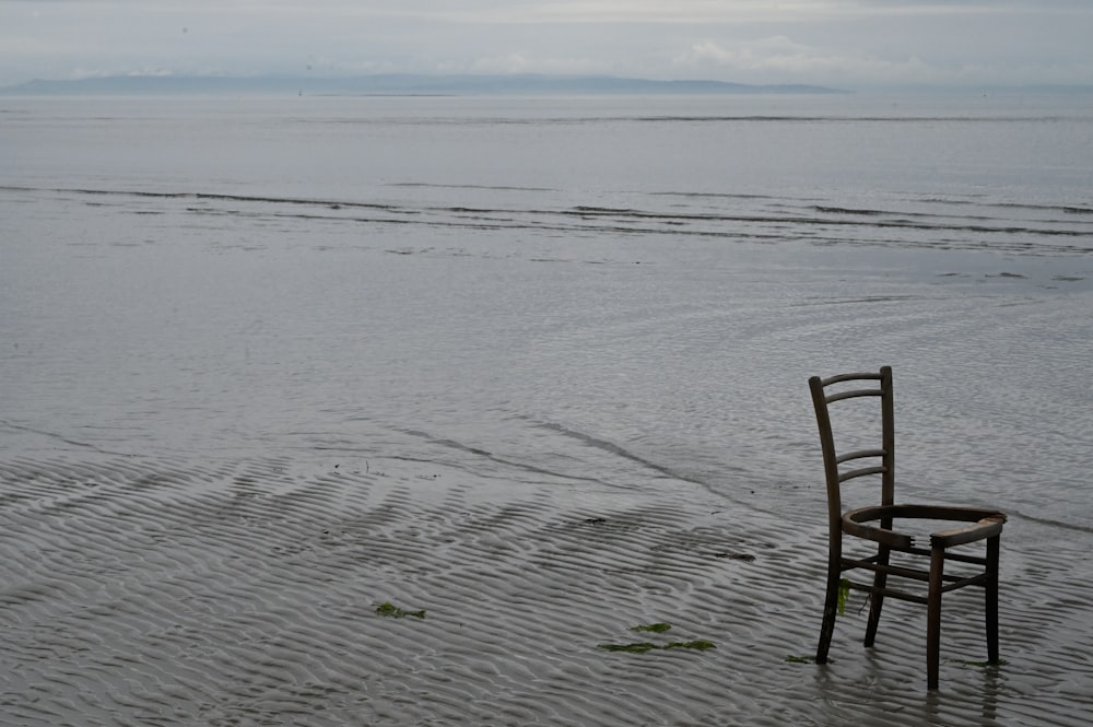 a wooden chair sitting on top of a wet beach