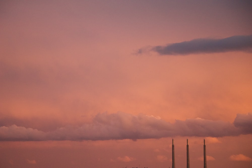 a pink sky with a few clouds and a row of smoke stacks in the distance