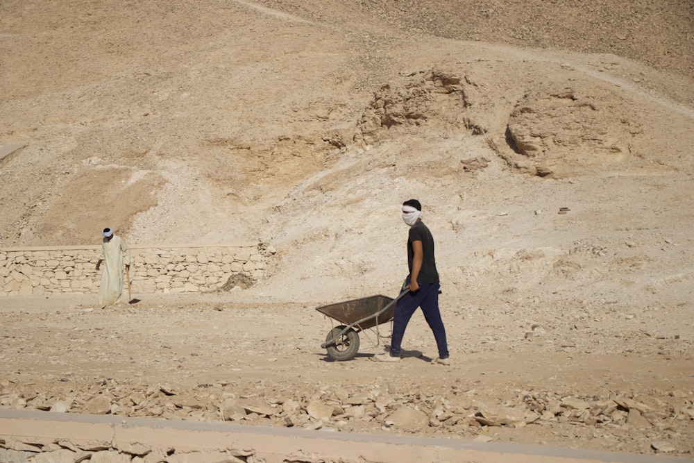a man walking in the desert with a wheel barrow