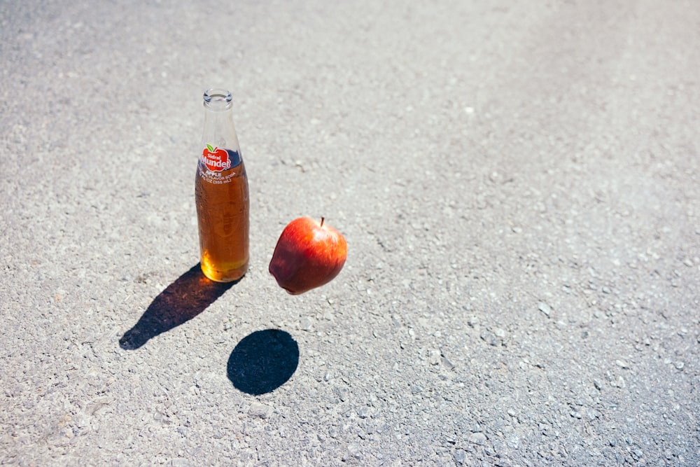 a bottle of soda and an apple on the ground