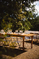 A long wooden table set outdoors with rustic plates and candles, surrounded by guests enjoying a sunny afternoon feast.