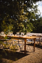 A rustic wooden table set outdoors under pine trees, with plates of fresh regional dishes and glasses of wine catching the golden sunset light.