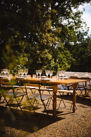 A long wooden table set outdoors with rustic plates and candles, surrounded by guests enjoying a sunny afternoon feast.