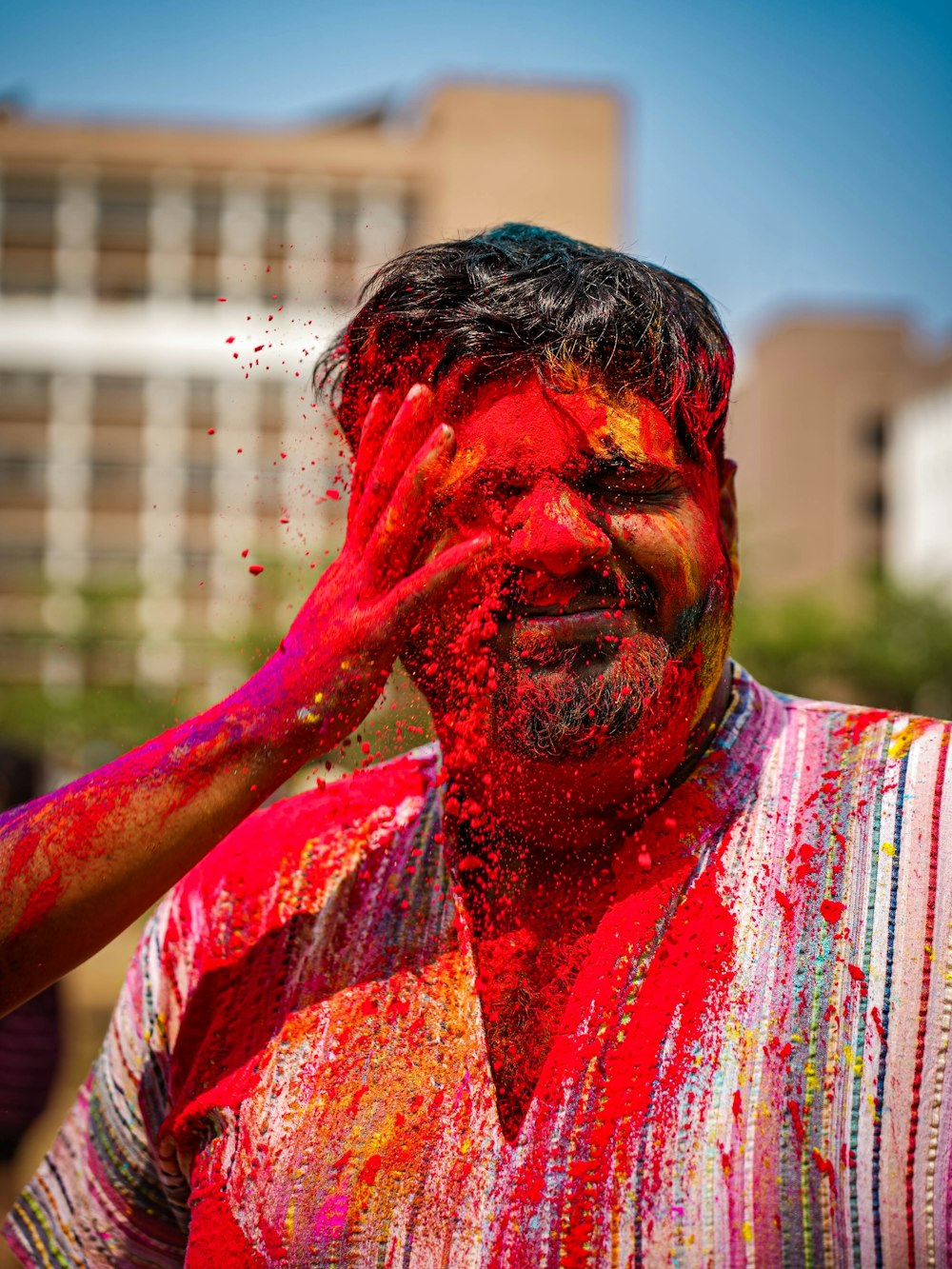 a man covered in colored powder with his hands on his face