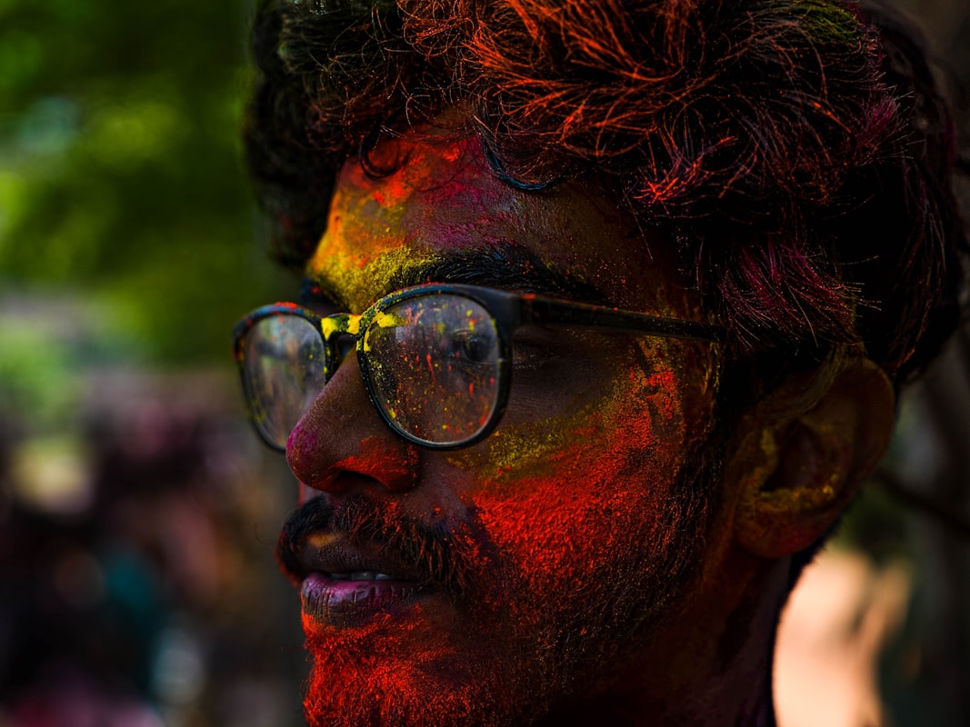 Man's face covered in colorful powder during Holi celebration. Photo by Devansh Bose on Unsplash.