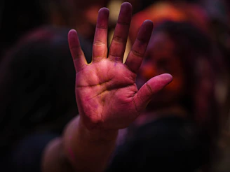 Close-up of hands covered in bright blue and green Holi colors, holding flower petals.