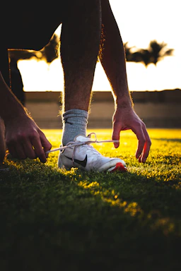 Runner lacing up sports gloves and ankle supports on a city trail at sunrise