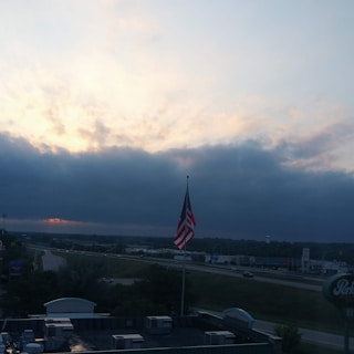 An American flag subtly waving behind a rugged semi-truck on a highway at sunset.