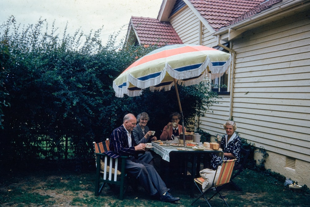 a group of people sitting around a table under an umbrella