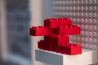 Red LEGO bricks are stacked in an abstract shape against a background of a LEGO baseplate.