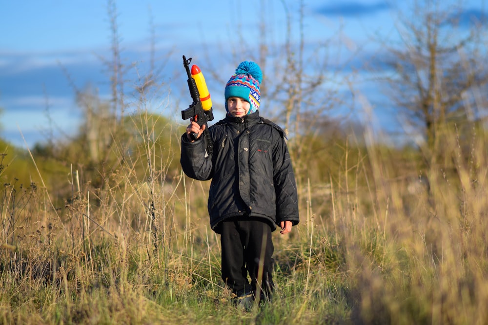 a young boy holding a toy gun in a field