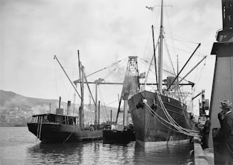 Black and white photo of a cargo ship docked at a busy port with containers being loaded.