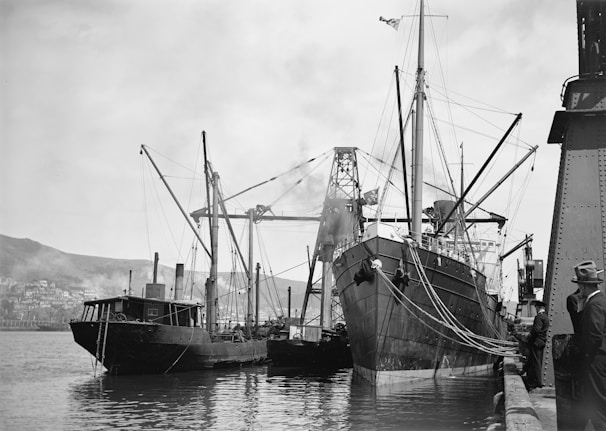 Black and white photo of a cargo ship docked at a busy port with containers being loaded.