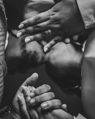 Intertwined hands display unity and connection in a monochromatic setting. A prominent engagement ring adorns one finger, highlighting a sense of commitment.