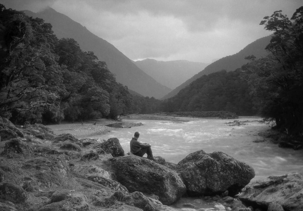 a man sitting on a rock next to a river