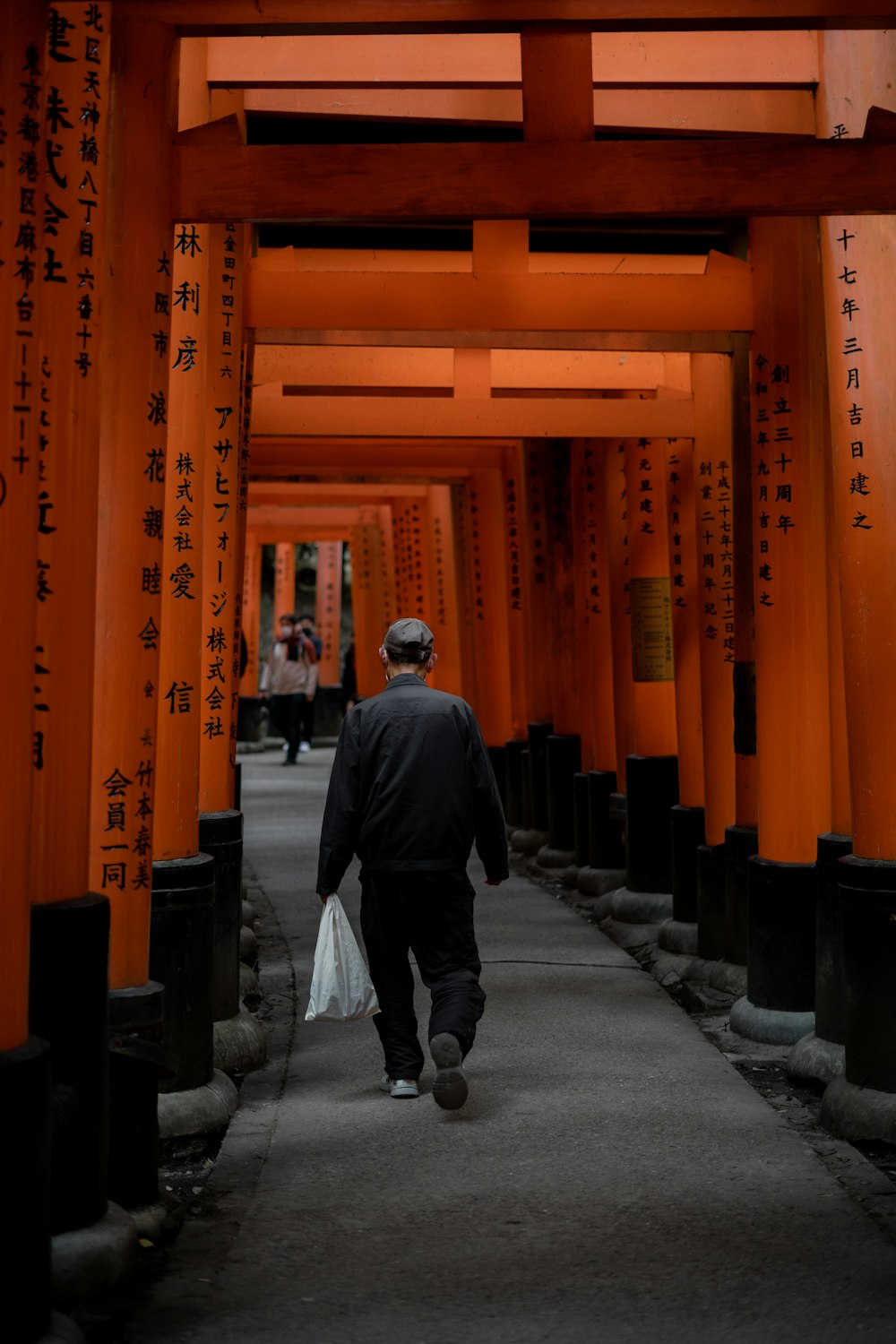 a man walking down a walkway between tall orange pillars