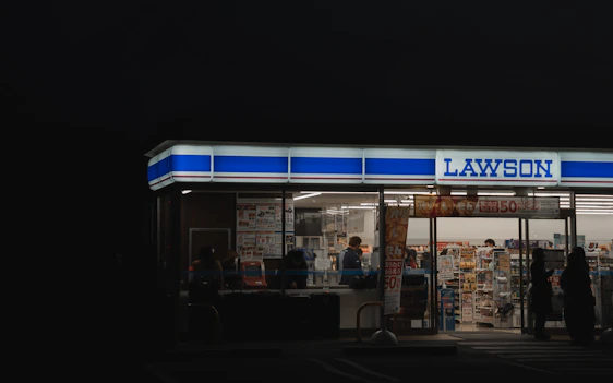 A cozy, brightly lit convenience store interior with red, white, and blue decor and smiling staff ready to help customers.