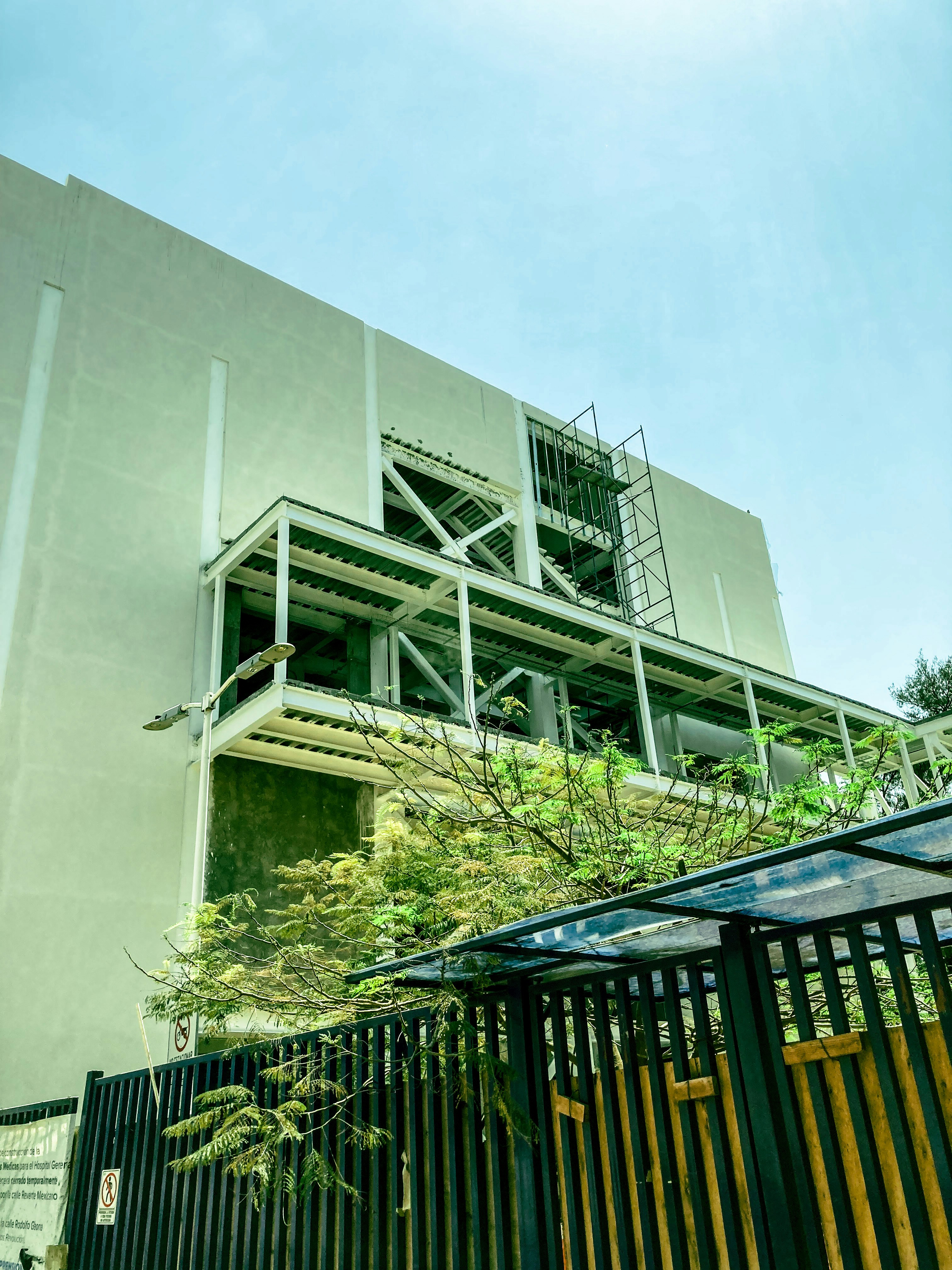 Modern multi-storey building under construction, scaffolding on all floors, bright daylight, clean architectural composition