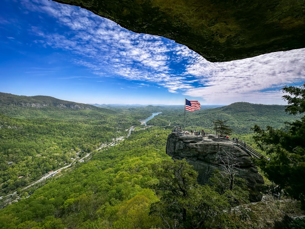 an american flag on top of a mountain overlooking a valley