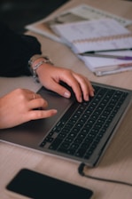 Hands typing on a laptop keyboard with a smartphone nearby