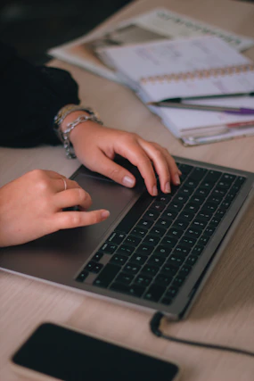 Close-up of hands typing on a laptop keyboard with network cables and a smartphone nearby.