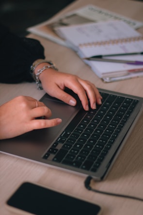 Close-up of hands typing on a laptop surrounded by coffee cups and notebooks.