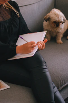 A playful dog curled up beside a mum journaling in a soft, quiet nook.