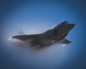 A sleek military jet is captured mid-flight against a clear blue sky, with vapor streaming off its wings, indicating high speed and aerodynamic performance.