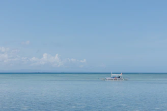 A sturdy fishing boat cutting through calm blue waters under a clear sky.