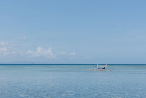 A sturdy fishing boat cutting through calm blue waters under a clear sky.