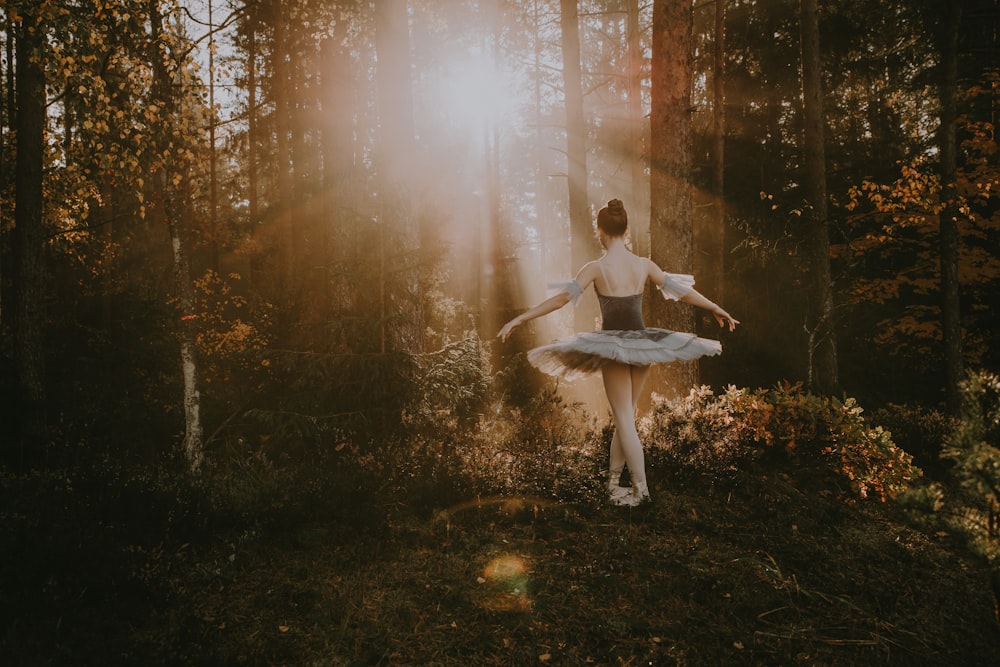 a woman in a white dress is dancing in the woods