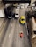 A top-down view of a multi-lane road with several vehicles including cars, a truck, and a motorcycle. The vehicles are mostly moving forward, with a yellow and green taxi and a red motorcycle standing out. The road is flanked by concrete sidewalks, and an overpass structure is visible in the upper part of the image.