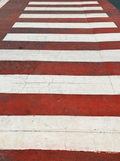 Alternating white and red stripes form a pedestrian crosswalk on a cracked asphalt surface.