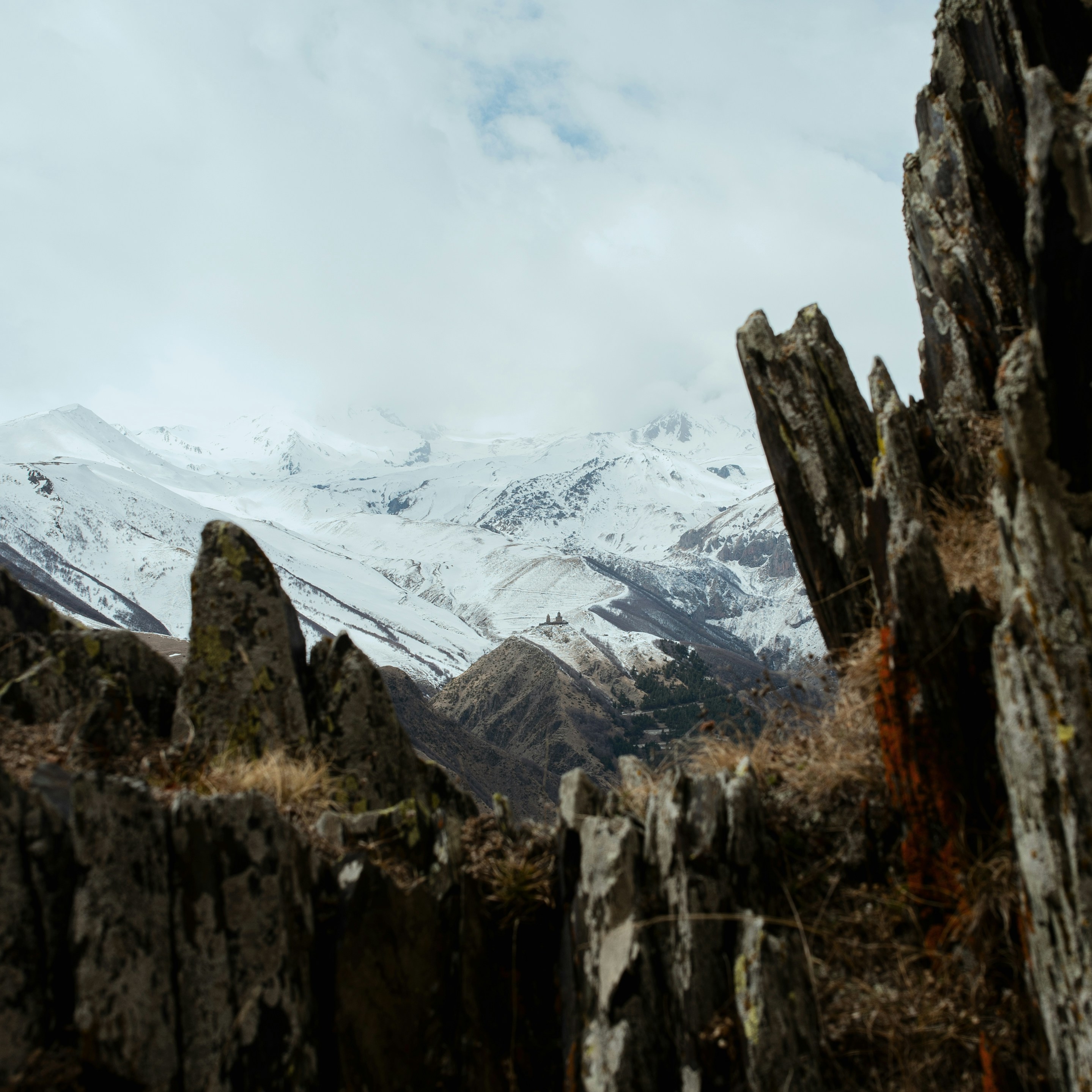 a view of a snowy mountain range from a rocky cliff