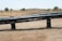 A dry landscape with brown grass and a few scattered trees is in the background. In the foreground, there are large black pipes elevated on supports, stretching horizontally across the image.