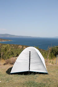 A sleek dark green tent set up on a sandy beach with a clear blue sky overhead.