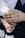 A close-up of a small child's hand gently placed on top of an adult's hand, which is wearing a gold band. The adult is dressed in a dark suit with a white shirt, and the child's sleeve is also white. The background is softly blurred, drawing focus to the hands.