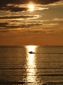 A serene boat gliding across a calm lake at sunset.