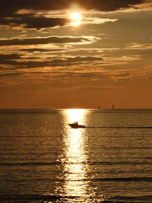A serene boat gliding across a calm lake at sunset.