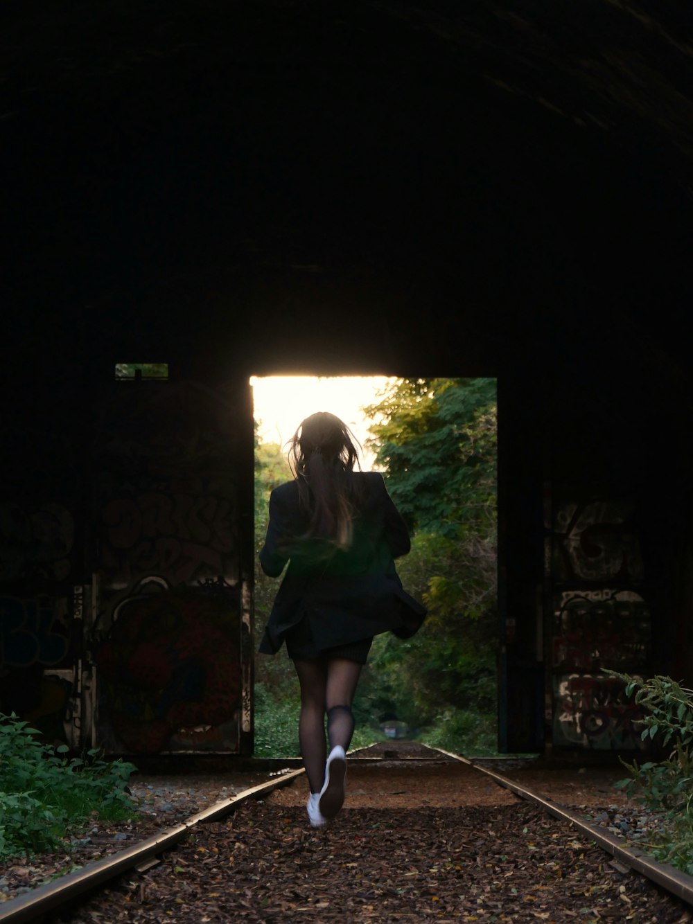 a woman in a black dress is walking through a tunnel