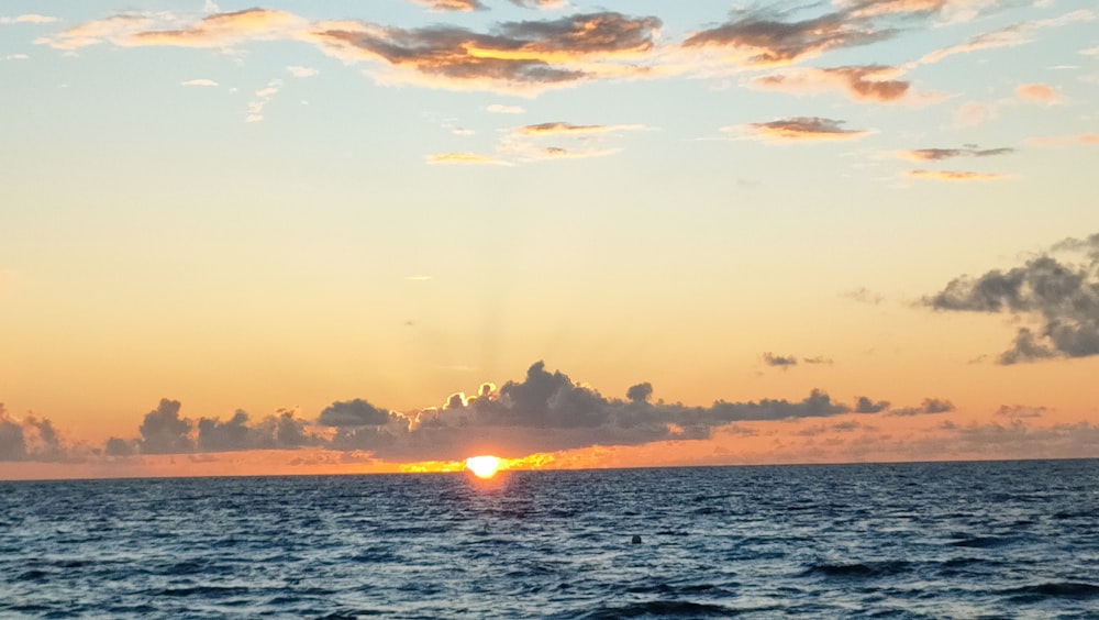 o sol está se pondo sobre o oceano em um dia nublado