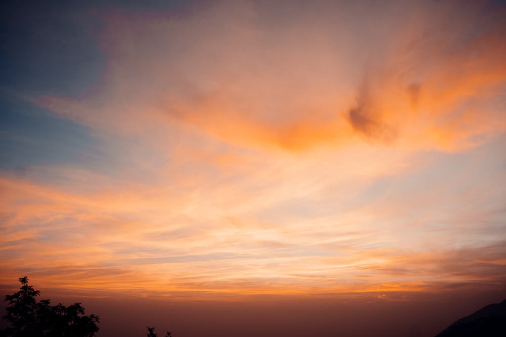 a sunset with clouds and trees in the foreground